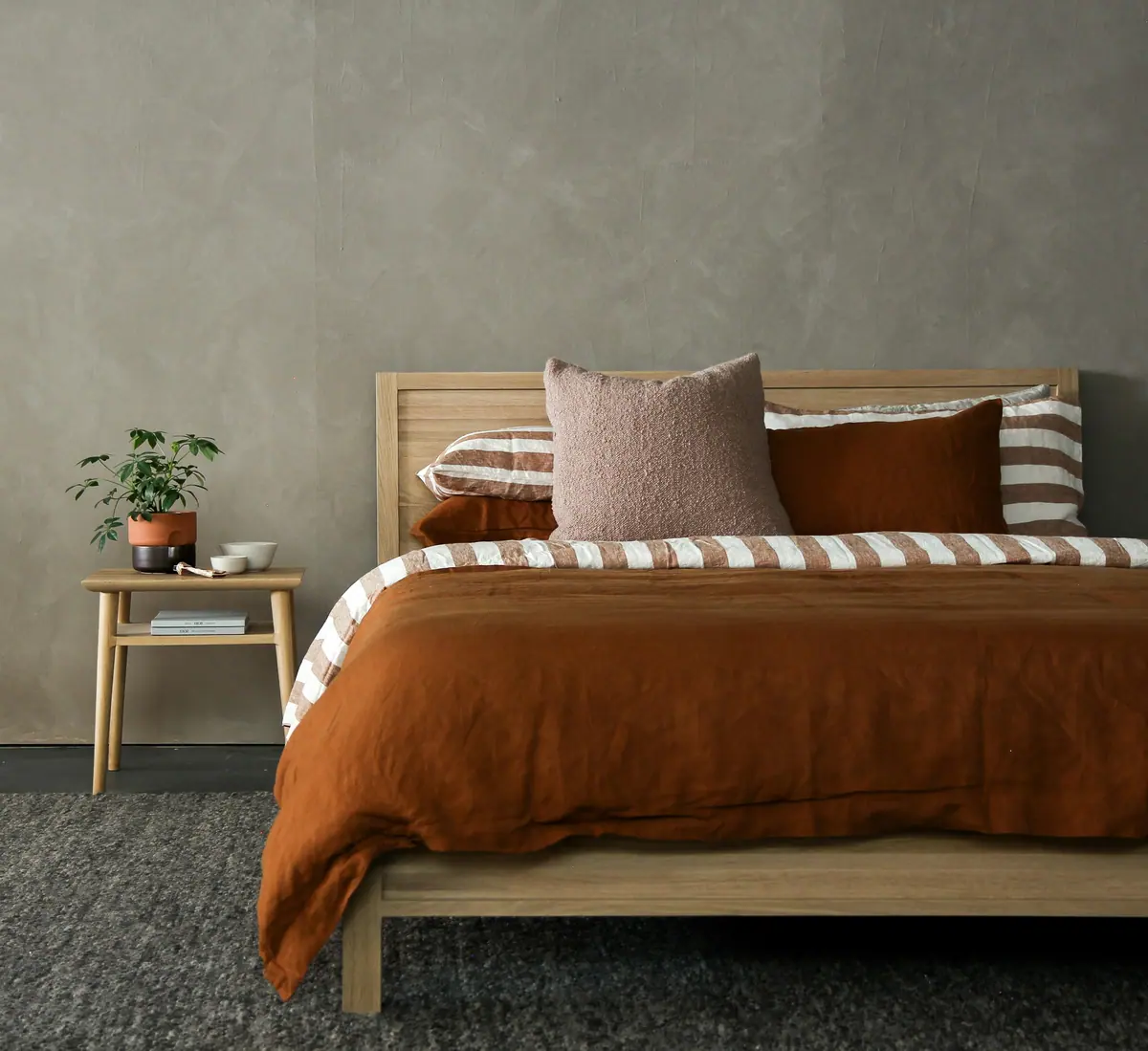 Suíte do Apartamento Íris com roupa de cama terracota e cabeceira em madeira